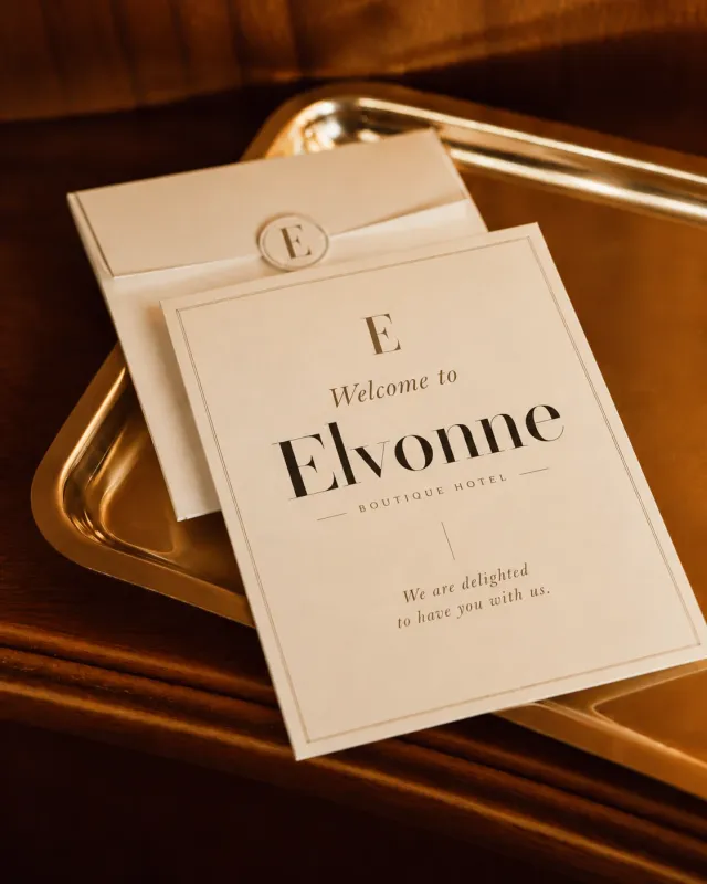 Velkomstkort «Welcome to Elvonne, Boutique Hotel» med E-segl på et messingbrett. KI-generert.