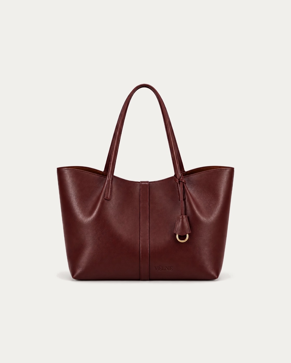 VÉLNE 01 Large Tote: burgunder skinnveske med to hanker, anheng med messingring og preget ordmerke. KI-generert.