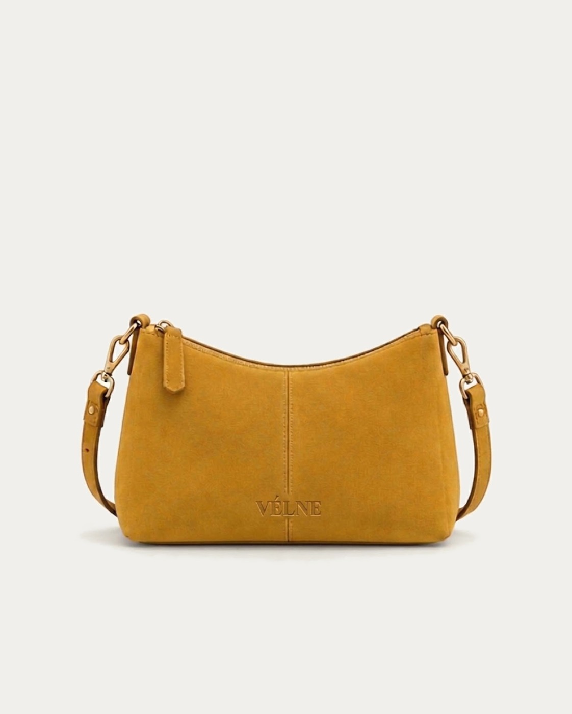 VÉLNE 03 Mini Crossbody: liten okerfarget veske i semsket skinn med preget ordmerke. KI-generert.